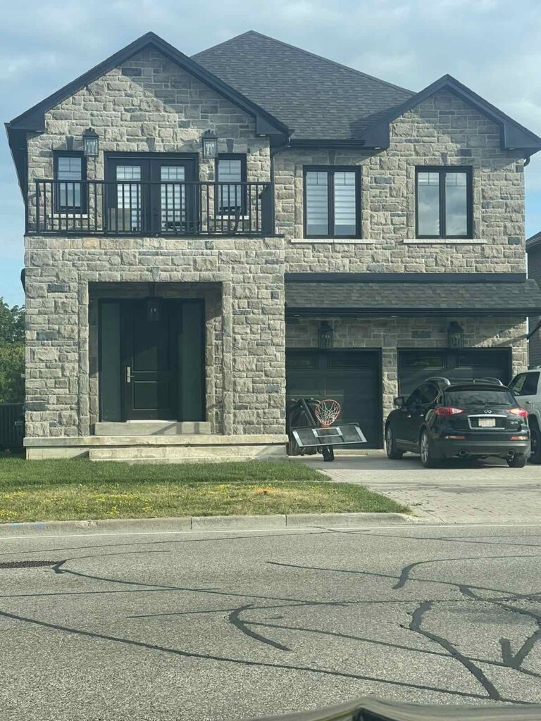 Black frame casement windows and black steel entry door installed on two-storey stone exterior home in Winnipeg