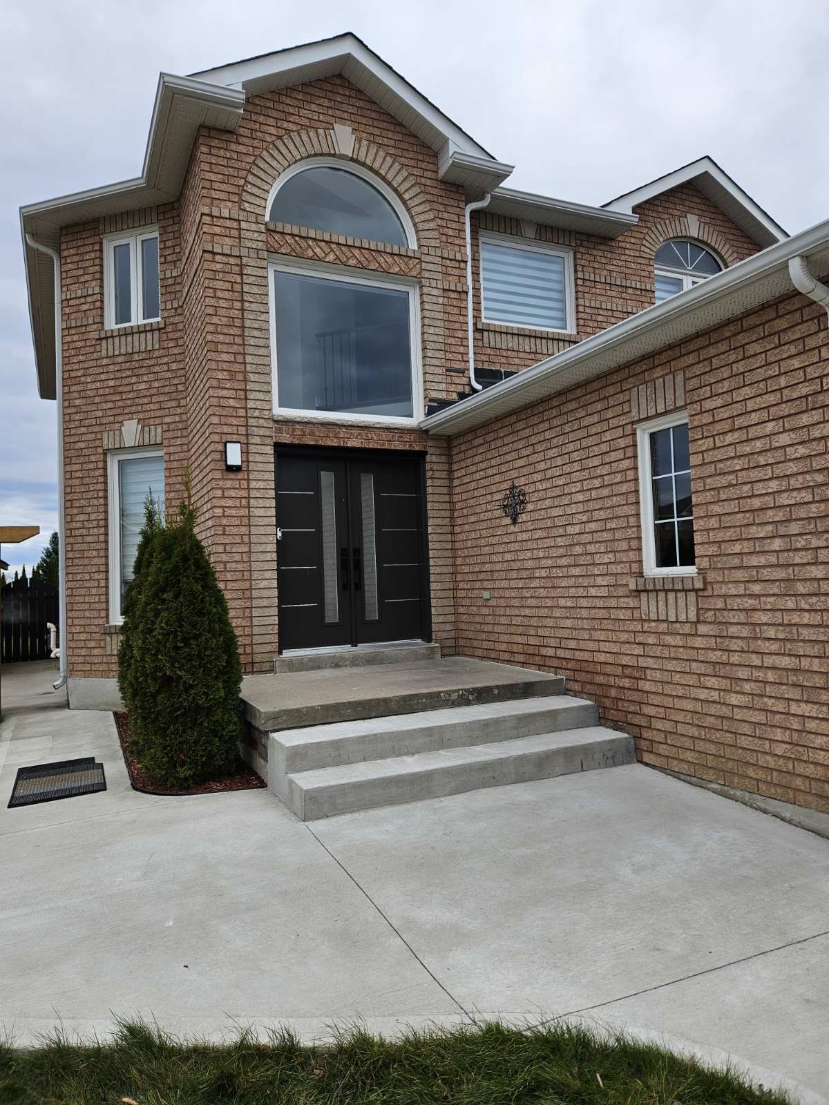 SmartTech complete window and door installation on Winnipeg brick home featuring black steel entry door, picture window, arched transom and casement windows