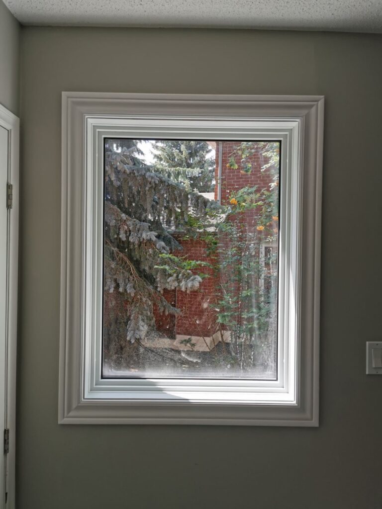White vinyl fixed casement window with decorative trim installed in Winnipeg home interior with winter garden view