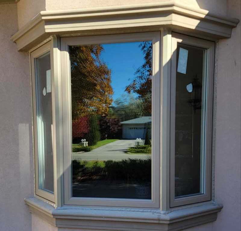 Newly installed energy-efficient bay window on residential stucco wall in Winnipeg reflecting autumn trees and driveway