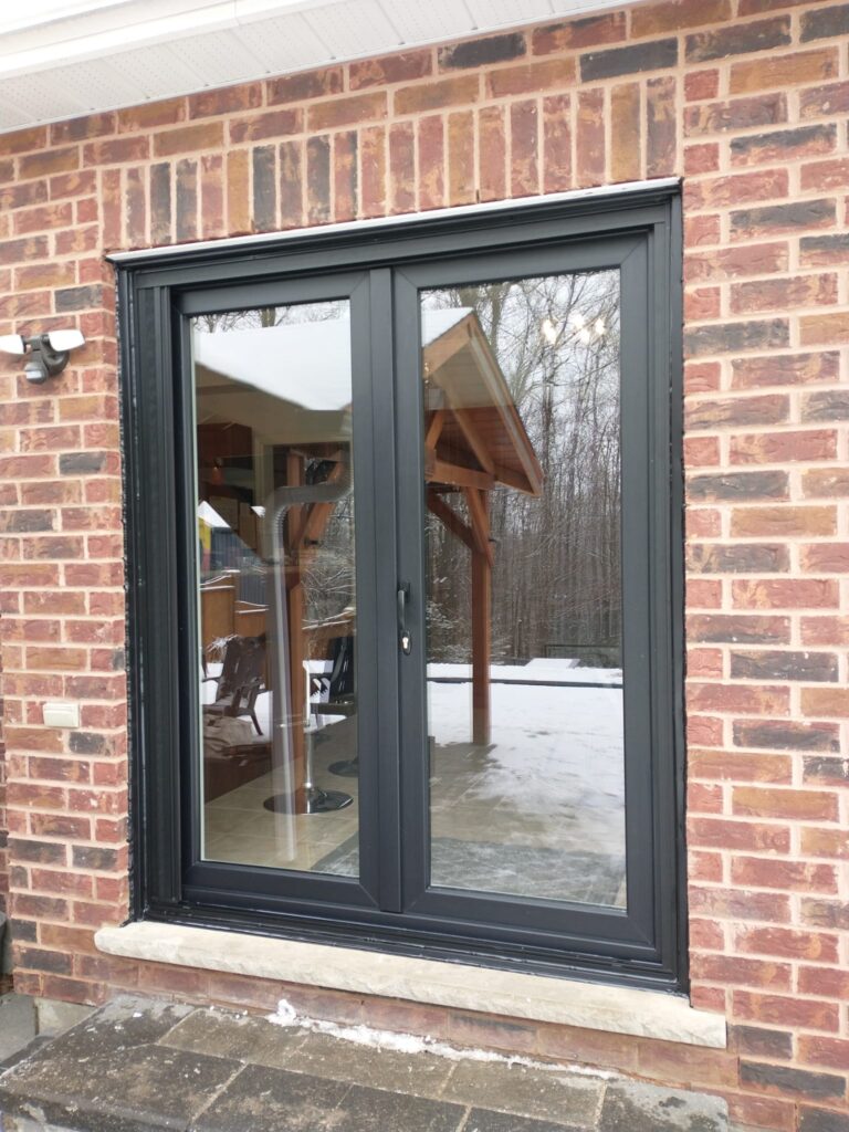 Black-framed double patio doors newly installed on red brick exterior wall of Winnipeg home during winter