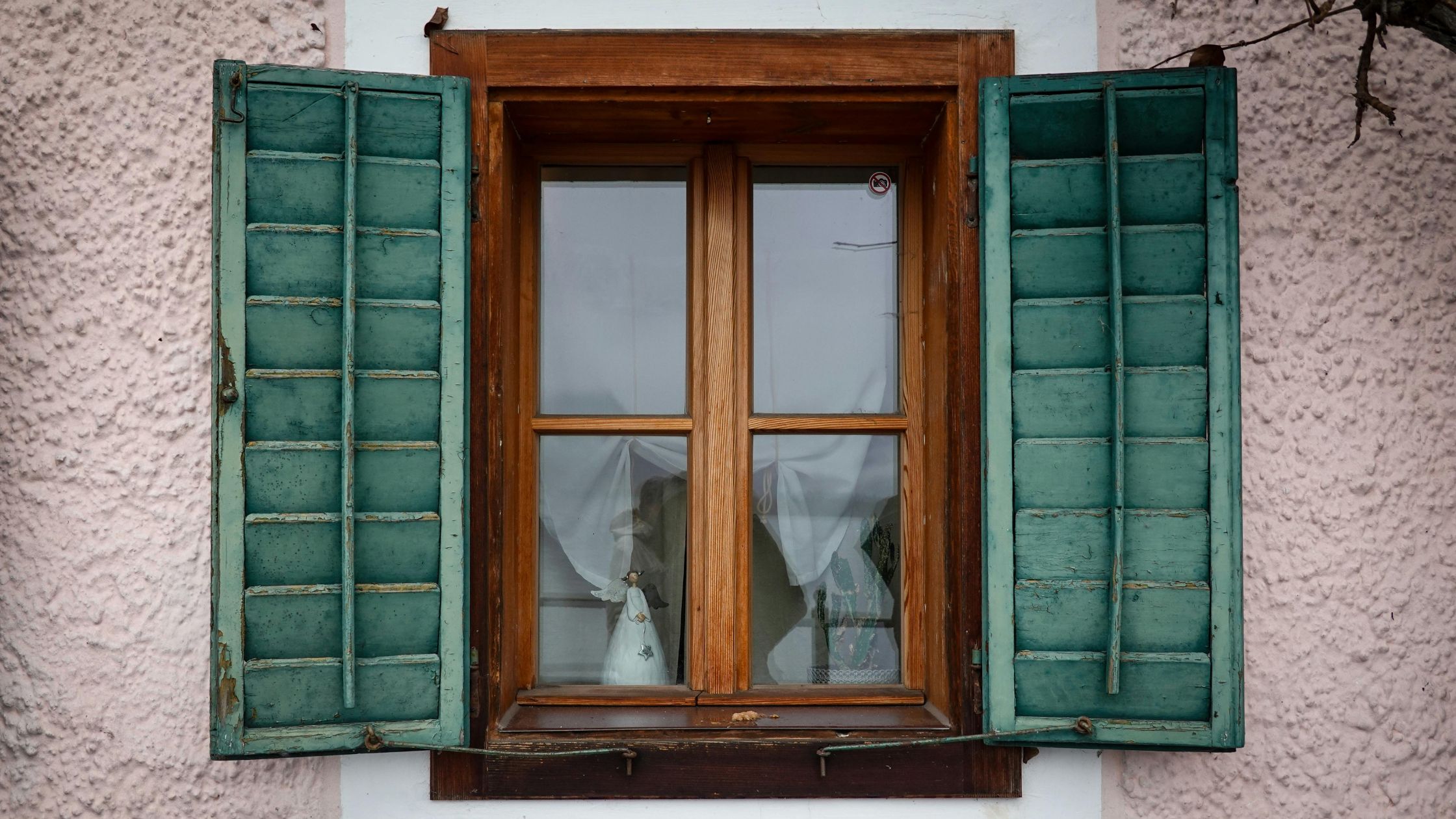 Common window problems in Winnipeg homes shown by an old wooden window with peeling paint, damaged shutters, and visible wear from harsh weather.
