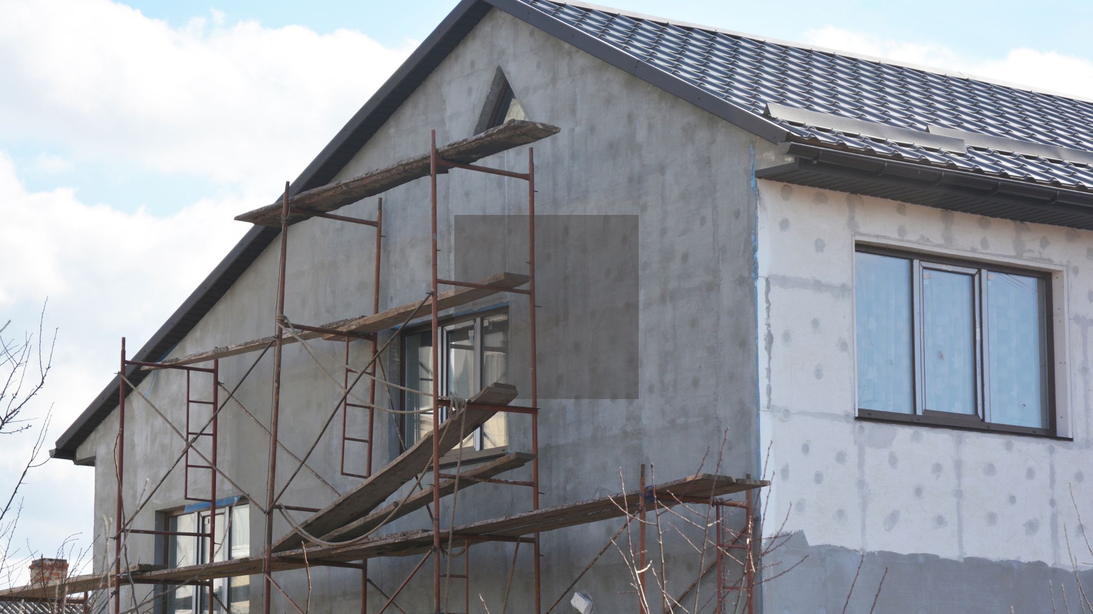 Exterior of a home under renovation with scaffolding and window installation in progress, showing ideal spring conditions, highlighting the best time of year to install new windows in Winnipeg.