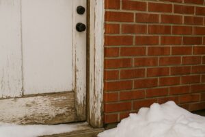 Damaged old exterior door with peeling paint and snow buildup in Winnipeg, showing signs it's time for energy-efficient door replacement.