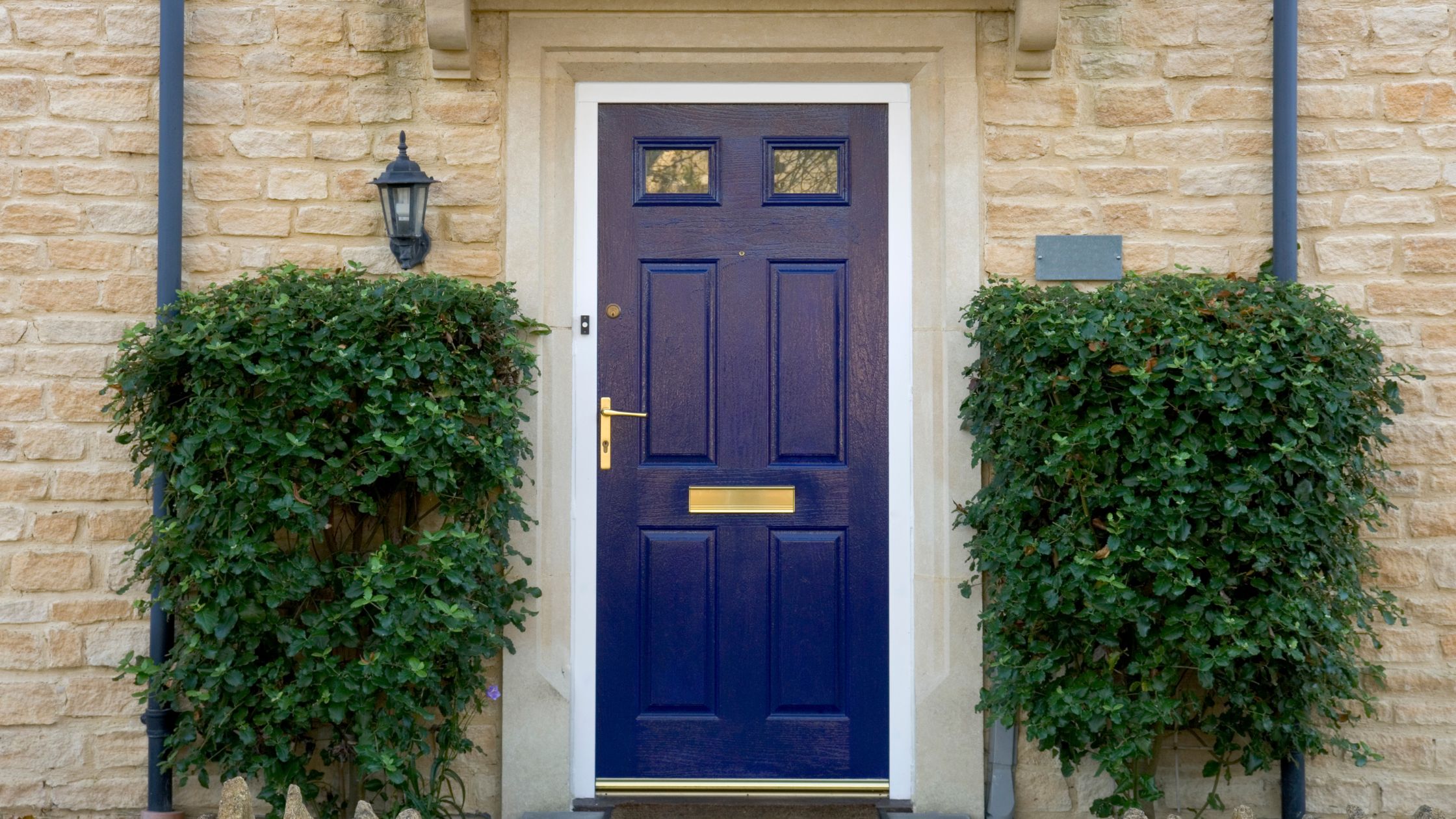 Entry Door Home Security with a solid navy blue front door featuring a brass handle and mail slot, surrounded by brick walls and green hedges in Ontario.